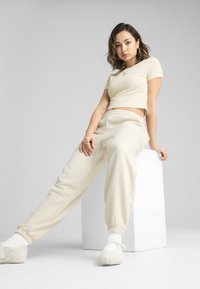 Krémový croptop a odpovídající jogger kalhoty s elastickými manžetami, doplněné o jedinečné texturované tenisky. Jednoduchý design, měkká látka, uvolněný střih.