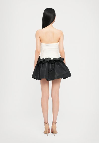Vestido sin tirantes que presenta un corsé blanco ajustado y una falda de satén negro voluminoso con un dobladillo con volantes, combinado con tacones transparentes.