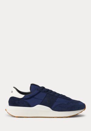 Marineblå og hvid sneaker med ruskind- og stofpaneler, snørelukning og beige gummisål vist i sideprofil.