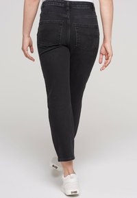 Jeans in denim nero con una forma aderente, vita media e tasche posteriori. Presentano cuciture sottili e orli cropped. Indossati con sneaker bianche.