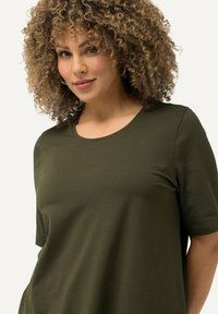 T-shirt verde oliva a maniche corte con collo rotondo. Il tessuto è morbido ed elastico, offrendo una vestibilità comoda.