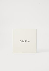 Vierkante witte doos met "Calvin Klein" in het zwart gedrukt, gecentreerd op een plain witte achtergrond.