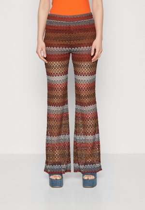 Pantalons évasés rayés marron et gris avec un design en tricot texturé, présentant des couleurs et motifs alternés, portés avec des talons plateformes en denim.