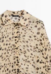Beige button-up shirt with black and brown irregular leopard spots and a classic collar.