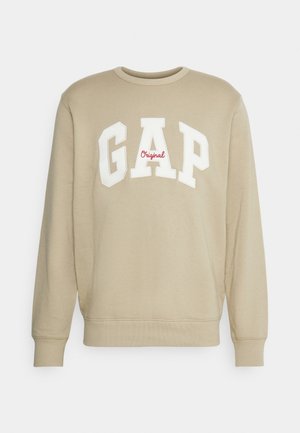 Beiger Langarm-Sweatshirt mit gerippten Bündchen an Ärmeln und Saum, vorne große weiße "GAP" Buchstaben und kleiner roter "Original" Text.