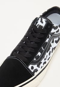 Les baskets en noir et blanc présentent un bout en daim, des côtés en toile à imprimé léopard, des lacets noirs, des coutures contrastées et une semelle en caoutchouc.