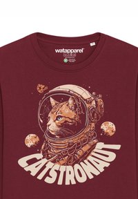 Bordeaux T-shirt met een grafisch ontwerp van een kat in een astronautenhelm, voorzien van de tekst "CATSTRONAUT" en ruimte-thema details zoals planeten en sterren.