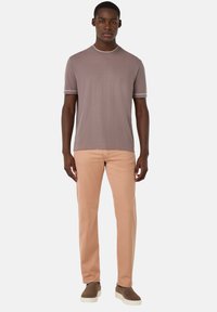 T-shirt a maniche corte di colore taupe con cuciture bianche, abbinato a pantaloni rosa chiaro e scarpe slip-on beige. Tessuto morbido, vestibilità casual.