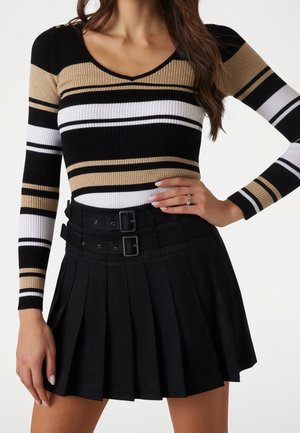 Femme portant un haut à manches longues rayé beige, noir et blanc avec une mini-jupe noire plissée avec des boucles de ceinture doubles.