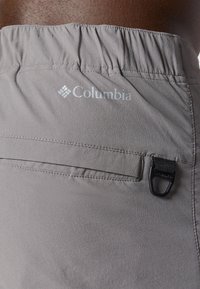 Pantalones cortos grises de Columbia con cinturilla elástica, bolsillo cosido y un lazo negro de sujeción. Tejido suave con una textura ligera.
