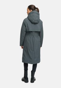 Long green parka coat with a cinched waist, hood, and embroidered detail on the back. Features two side pockets and a smooth texture.