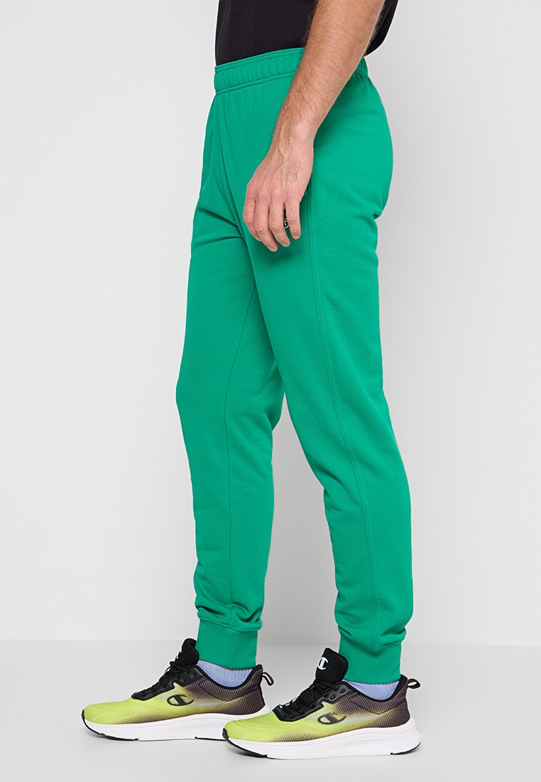 Pantalones deportivos verdes hechos de una tela suave, con una cintura elástica, diseño de pierna ajustada y costuras laterales sutiles. Combinados con zapatillas de colores.