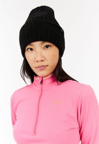 Czarna, prążkowana czapka beanie o usztywnionym wierzchu. Noszona z jasnoróżową bluzą na zamek, która ma złote logo i akcent w postaci kołnierza.