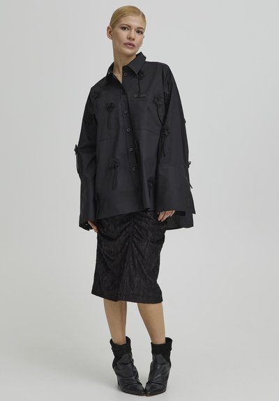 Sort oversized skjorte med blomsterapplikationer og knapper foran, kombineret med et rynket sort skørt og slappe sorte ankelstøvler.