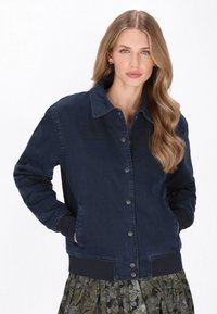 Tengerészkék farmerdzseki gombos elejével, bordás mandzsettákkal és zsebekkel; gallérral és sima textúrával rendelkezik.