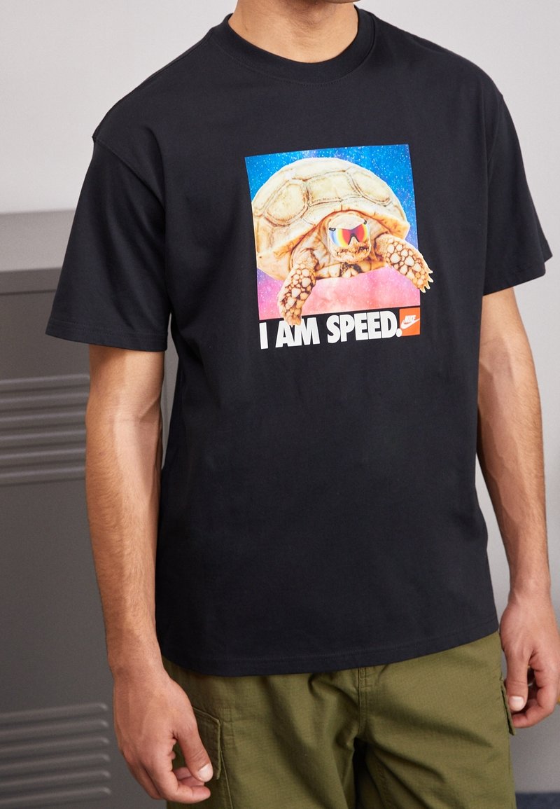 Camiseta de algodón negra con un gráfico colorido de una tortuga con gafas de sol y el texto "SOY VELOCIDAD" en letras blancas en negrita.