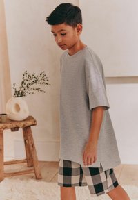 Grå t-shirt med kort ärm och avslappnad passform samt lätt struktur, i kombination med svartvitrutiga shorts. Enkelt design, utan ytterligare detaljer.