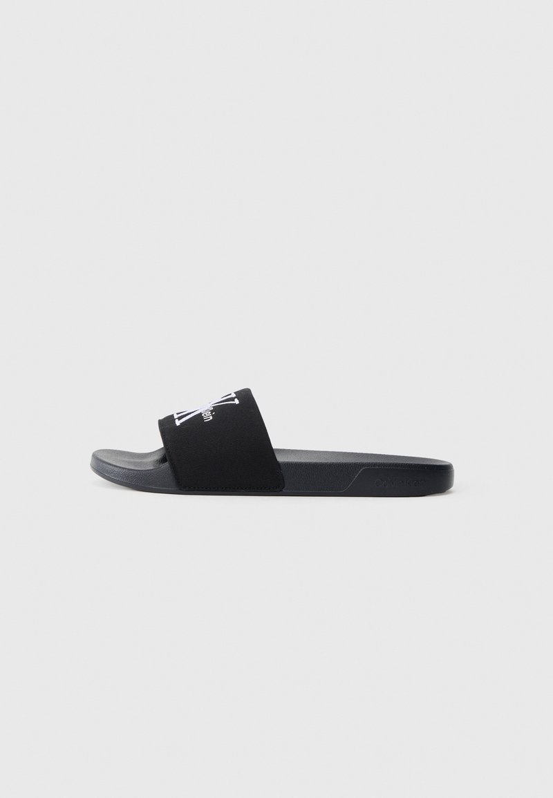 Black slide sandal made of rubber with a flat sole. Features a wide upper strap and a printed logo on the strap. Minimalist design.