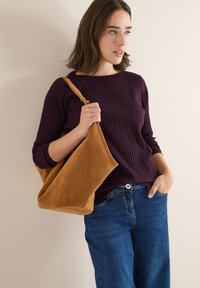 Brun svinskinns axelväska med en mjuk, slät textur, kombinerad med en ribbad mörklila topp och blå jeans. Enkelt design med inga synliga mönster.