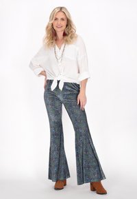 Witte, knoopblouse geknoopt in de taille; uitlopende, paisleypatroon broeken in blauw en groen; bruine, enkellaarsjes met hak.