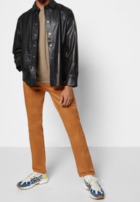 Czarna skórzana koszula na guziki, beżowy pasiasy t-shirt, pomarańczowe spodnie oraz wzorzyste sneakersy z niebieskimi, białymi i żółtymi akcentami.