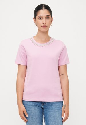 Lys rosa t-skjorte med korte ermer og rund hals, dekorert med klare, prydperler, sammen med blå jeans.