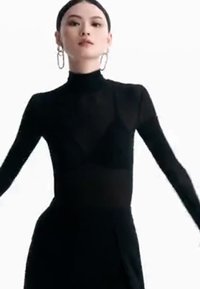 Svart langermet bodysuit med høy hals, med gjennomskinnelige paneler og en tettsittende silhuett, kombinert med store hoopsølvøreringer.