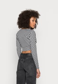 Top cropped de mangas longas em padrão xadrez preto e branco, com tecido elástico, gola redonda e design ajustado. Combinado com jeans pretos de cintura alta.