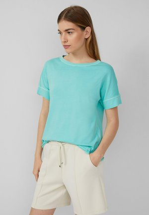 Light blue short-sleeve t-shirt made of soft fabric, featuring a relaxed fit and contrasting stitching details. Paired with beige shorts.