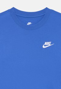 Jasne modré tričko s krátkym rukávom a bielym logom Nike na ľavej strane hrudi, zobrazuje výstrih a textúru tkaniny.