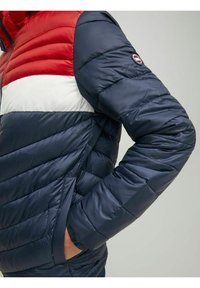 Zateplená bunda v červeném, bílém a námořnickém barevném provedení; vyrobena z hladkého, lehkého materiálu se zapínáním na zip a bočními kapsami.