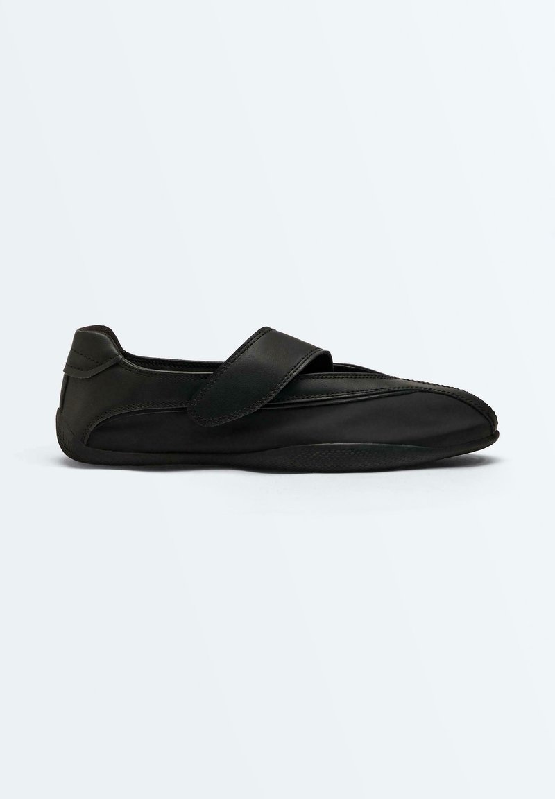 Chaussure adaptive en cuir noir avec une large bride en Velcro et une semelle flexible, conçue pour un enfilage facile et un confort optimal.