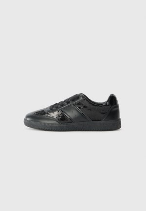 Lavtop sort sneakers med glansfulde og matte paneler, sorte snørebånd og tekstureret sål, vist i sideprofil på en ensartet lysegrå baggrund.