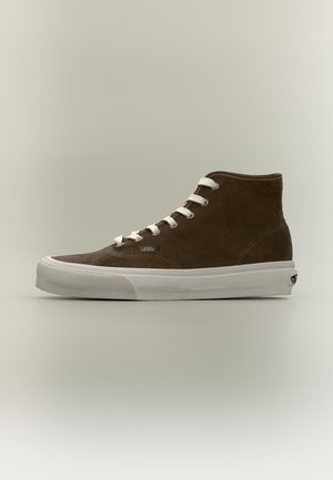 Baskets montantes en daim marron avec lacets blancs et épaisse semelle en caoutchouc blanche, vues de profil sur un fond uni.