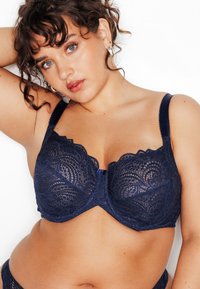 Reggiseno in pizzo blu navy con motivo floreale intricato, supporto con ferretto, bordi smerlati e spalline regolabili, con chiusura centrale a gancio.