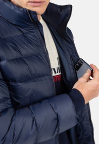 Giacca imbottita blu navy con colletto alto e chiusura a zip. Presenta polsini a coste e una tasca interna per riporre uno smartphone.