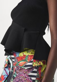 Haut noir sans manches côtelé avec peplum, associé à une jupe patchwork colorée présentant des motifs floraux, rayés et cachemire, avec une fermeture éclair à l'avant.