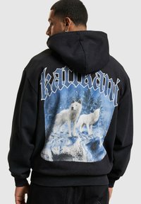 Sort hætte sweatshirt med et stort grafik af to hvide ulve mod en blå og snedækket baggrund. Ribstrikkede manchetter og kant.