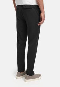 Svarte bukser med smal passform, med to baklommer med glidel�ås, elastisk midjebånd og rette ben. Kombinert med grå slip-on sko.