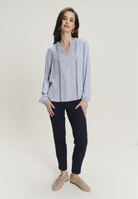 Blusa azul claro de manga larga con escote en V, tela texturizada, rayas verticales y puños recogidos, combinada con pantalones oscuros de color navy.
