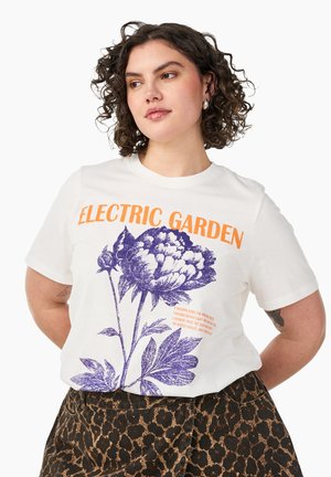 Kvinde med krøllet hår iført en hvid "Electric Garden" T-shirt med et stort lilla blomstergrafik og leopardprint nederdel.