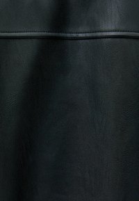 Svart läderytan med fin korntextur och en horisontell söm som löper över den övre tredjedelen av materialet.