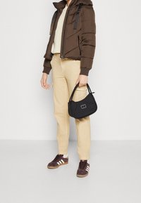 Brown puffer jacket with a hood, cream knit top, beige cargo pants, and dark sneakers. Holding a small black bag with white accents.