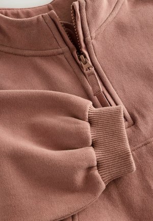 Maglione con zip in morbido tessuto rosa polveroso. Presenta polsini e colletto a costine con texture liscia. Cuciture decorative e design a mezza zip.