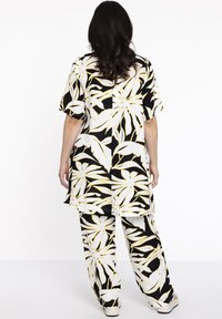 Zwart-wit outfit met een bladpatroon en gele accenten. De top heeft korte mouwen en de losvallende broek heeft een bijpassend ontwerp.