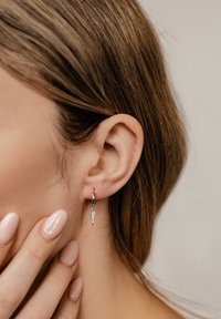 Boucles d'oreilles en argent, avec un design en chute pointue mettant en avant un accent en pierre précieuse transparente, présentées sur un fond neutre et des cheveux doux.