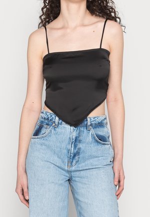 Mujer con un camisole de satén negro con dobladillo puntiagudo, tirantes finos y jeans vaqueros de tiro alto en azul claro.