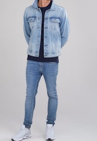 Jasnoniebieska kurtka dżinsowa z dwoma kieszeniami na piersi, w połączeniu z ciemnoniebieskim t-shirtem i jasnoniebieskimi jeansami o dopasowanym kroju, uzupełniona białymi trampkami.