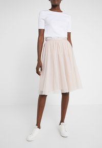 Falda de tul rosa claro con cintura fruncida y patrón de lunares blancos; combinada con una camiseta blanca de manga corta ajustada y zapatillas blancas.