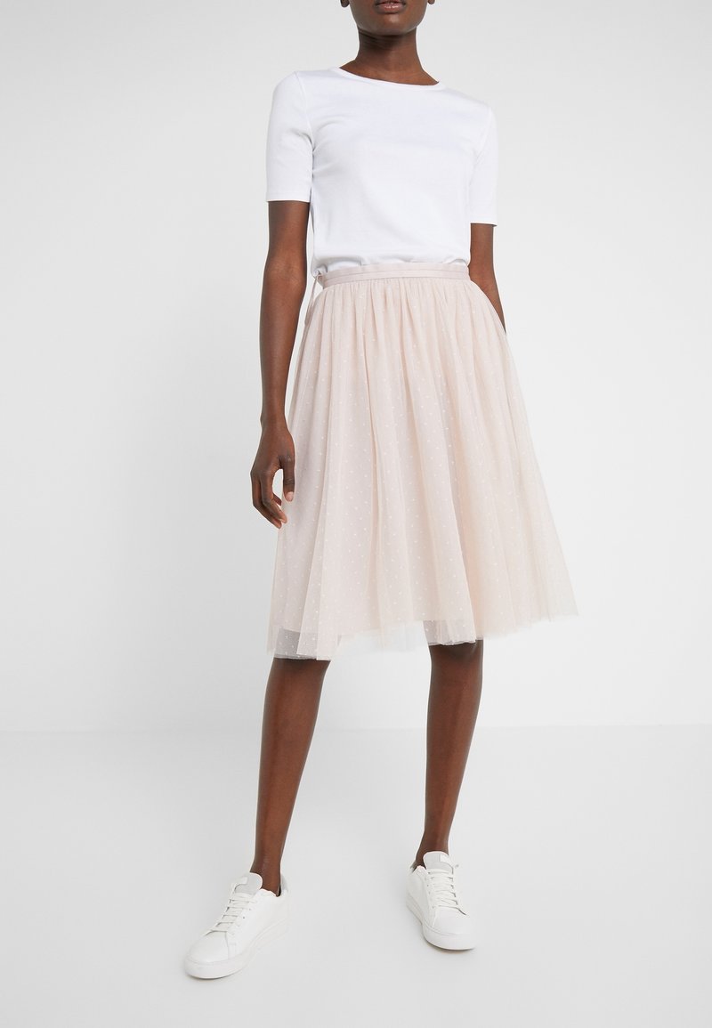 Falda de tul rosa claro con cintura fruncida y patrón de lunares blancos; combinada con una camiseta blanca de manga corta ajustada y zapatillas blancas.